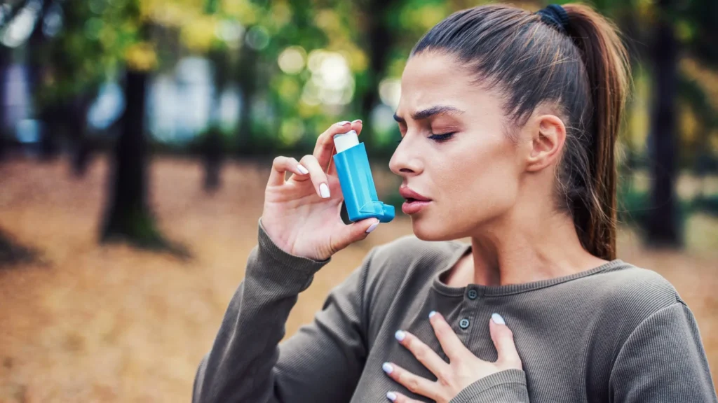 Woman using asthma inhaler, holding it up to her mouth with eyes closed