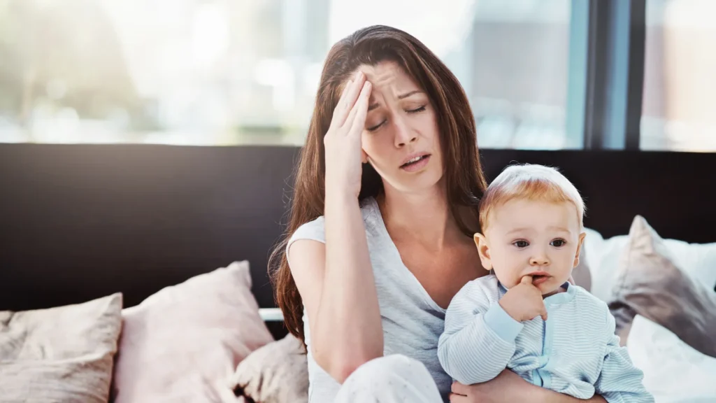 A woman gently holds a baby while suffering from lactation headaches 