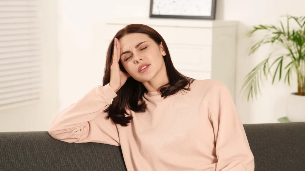 A woman sitting on a couch with her head in her hands, looking distressed.