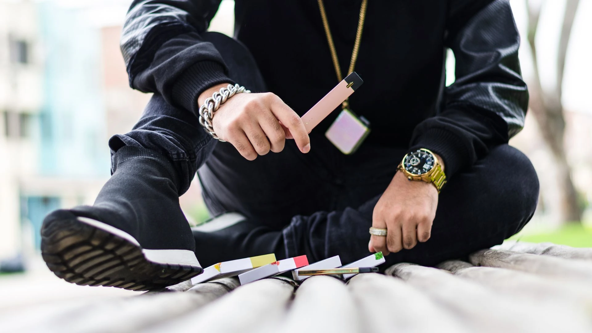 Do lungs recover from vaping?  A Young adult sitting outdoors holding a vape pen with multiple e-cigarette pods spread on the bench