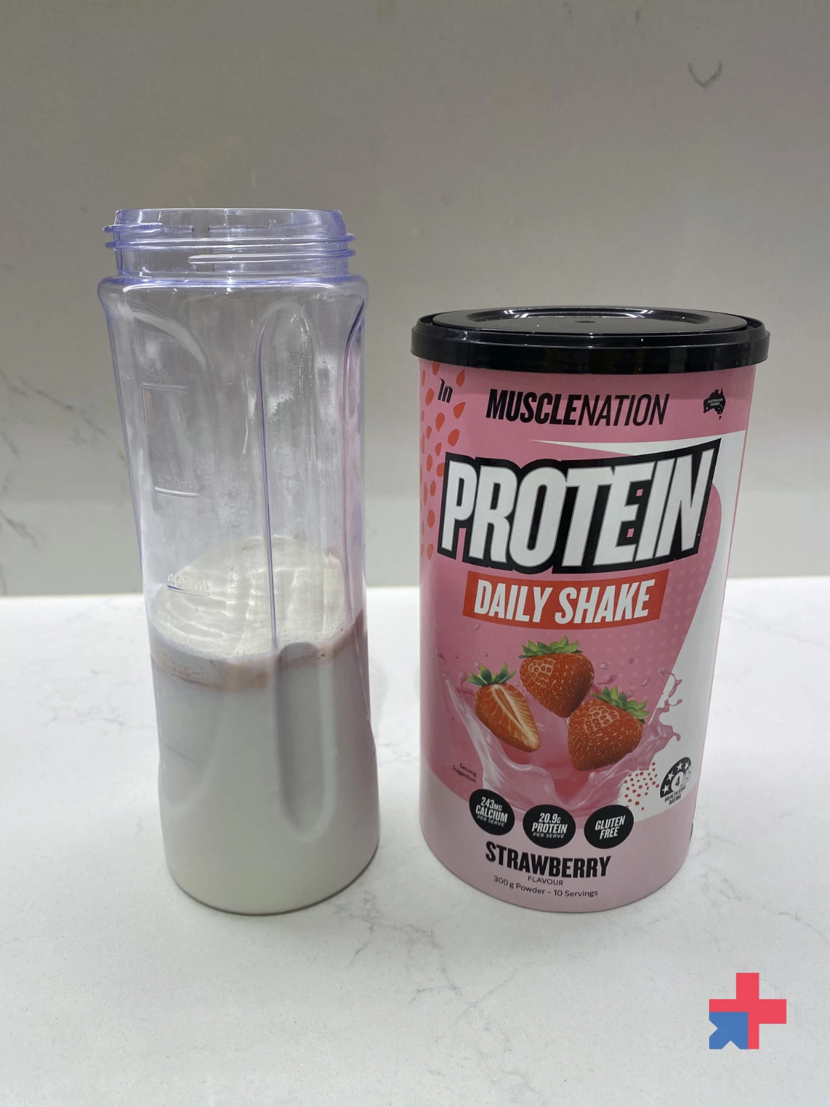 Bottle with milk and powder next to Muscle Nation Protein Daily Shake Strawberry tub on a white bench