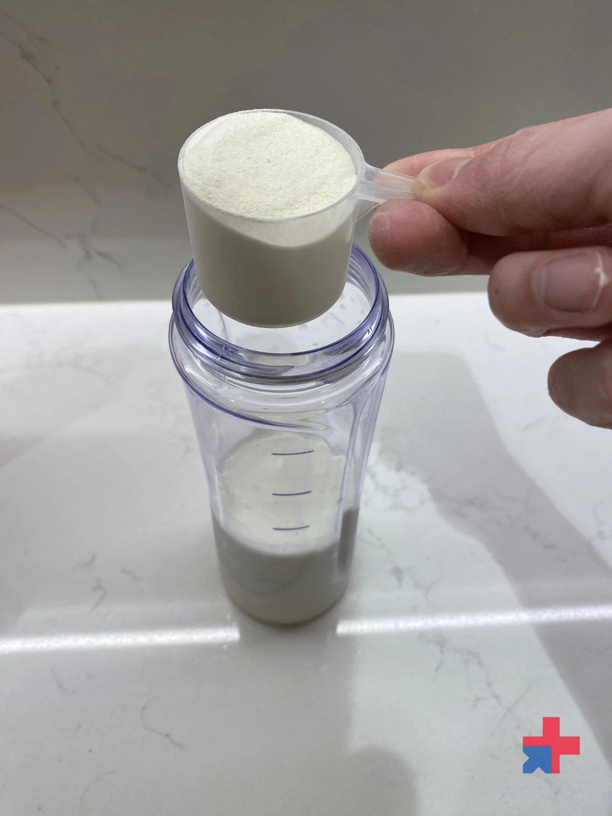 Scoop of Muscle Nation protein powder being poured into a shaker bottle filled with milk