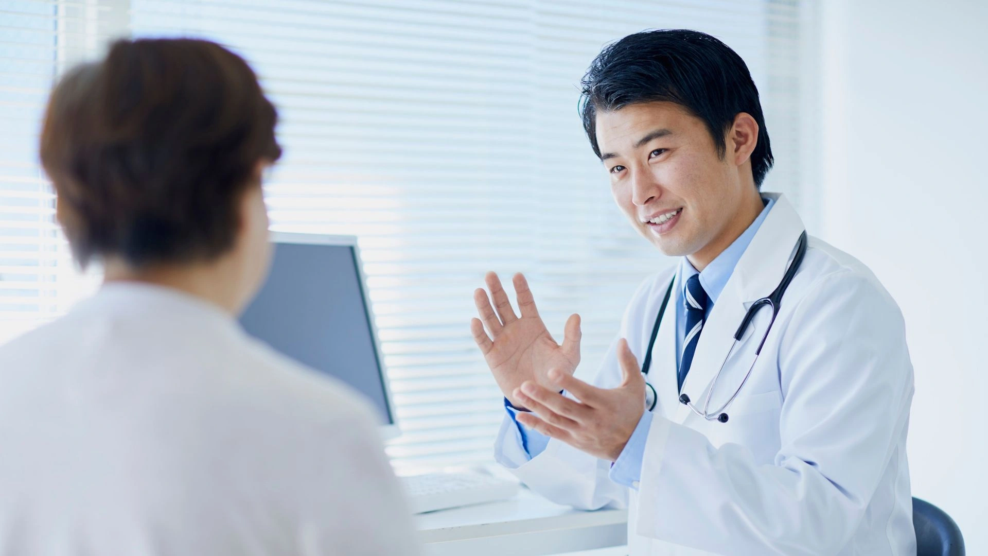 Male doctor in white coat speaking with a patient in a Singapore medical clinic. Early diagnosis and medical consultation are important for managing whooping cough and preventing complications.