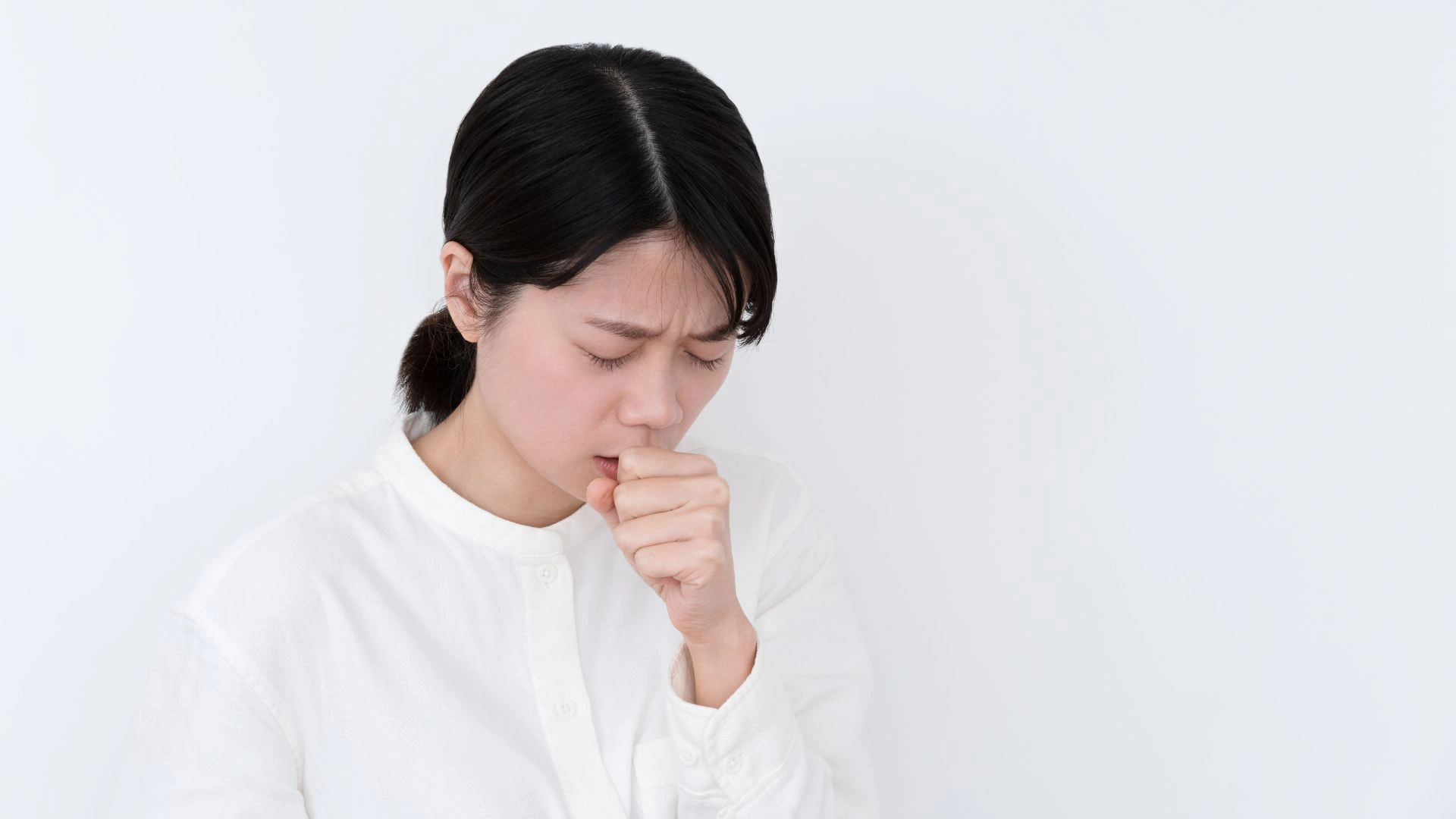 Woman with a painful coughing episode, illustrating the intense coughing characteristic of whooping cough. Prompt medical attention is recommended if symptoms appear in Singapore.