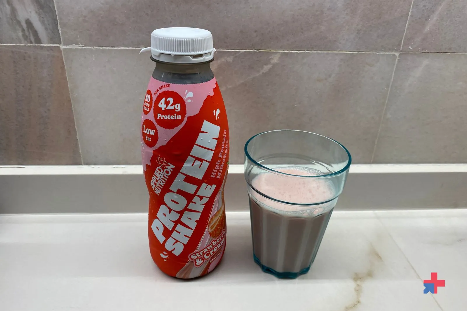 Applied Nutrition High Protein Shake Strawberry & Cream flavour 500ml bottle next to a glass filled with the pink protein shake